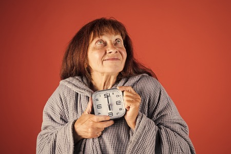 old age is inevitable. Old lady with red clock on red background.の写真素材