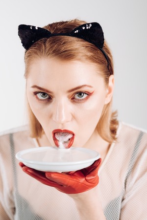 Ecology product and heath. Cat woman eat sour cream. Sexy cat woman lick milk from plate. Food and drink. Girl in kitten ears and red gloves with yoghurt isolated on white. Dieting and health.の写真素材