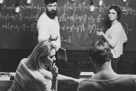 Bearded teacher, lecturer, professor watching students during test, exam, lesson. Students, group mates speaking, asking for advice or cheating while teacher watching them. Cheat on test conceptの写真素材
