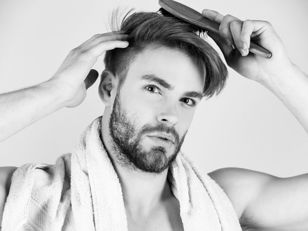 man takes care of his hair. Bearded man with bathing towel on neck combing healthy hair