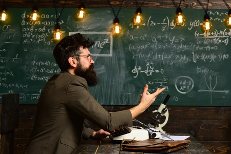 Man sits at table with books and writes. Scientist, teacher and student. Homework or lesson on chalkboard backgroundの写真素材