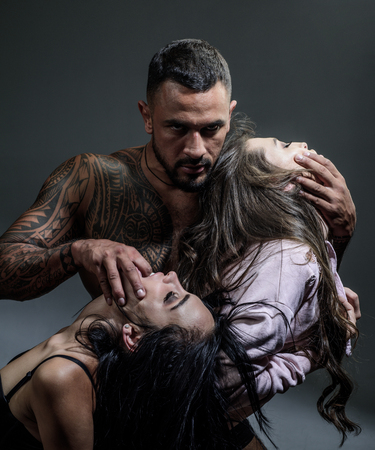 Sexy man playing on sensual girls abs, bigamy. Sensual sex and prelude. Orgasm and oral sex. Fetish concept. Role game with two sexy woman. Bdsm.の写真素材