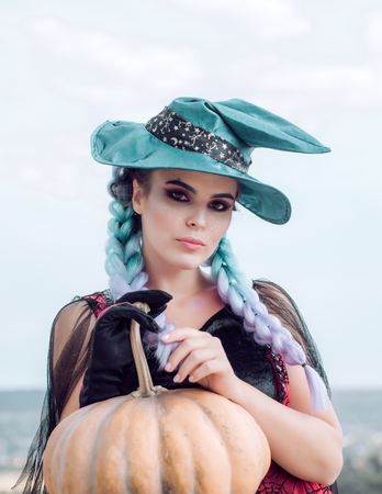 Woman posing with Pumpkin. Halloween Witch with in magic hat. Beautiful young surprised woman in witches hat and costume holding pumpkin. Attractive model girl in Halloween costume.の写真素材