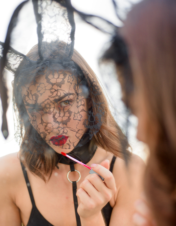 Sexy woman with bunny ears colors lips with red lipstick. Bunny rabbit easter concept. Sensual woman are getting ready for easter holiday.の写真素材