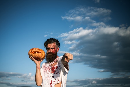 Halloween man pointing finger with pumpkin on cloudy blue sky. Vampire or zombie hipster bleeding with red blood. War, evil and horror. Holiday celebration conceptの写真素材