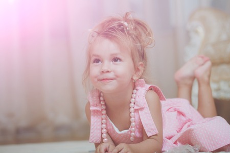 Child with cute smile in pink dress lie on carpetの写真素材
