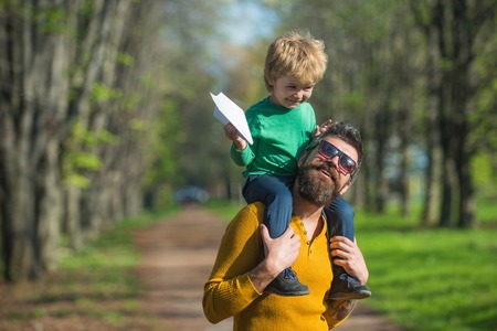 Traveling by plane. Small child boy on fathers shoulder launch paper plane in park, traveling concept. Flying better than everの写真素材
