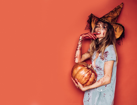 Halloween girl with a carved Pumpkin. Beautiful young surprised woman in costume holding pumpkin. Halloween Witch with pumpkin. Sexy vampire woman with blood on her face. Halloween party art design.の写真素材