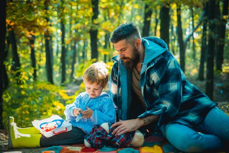 Cute little boy with his father during stroll in the forest. Father playing with little son on a picnic in the park in early autumn day.の写真素材