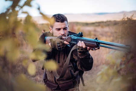 Hunter aiming rifle in forest. Hunter with shotgun gun on hunt. Track down.