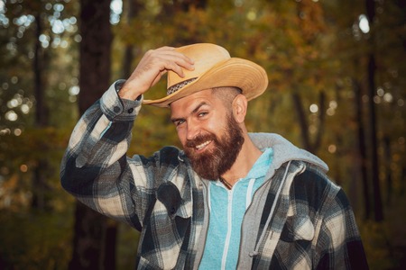 Happy young man are preparing for autumn sunny day. Portrait of handsome funny man with beard. Fashion portrait of beautiful sensual man in cowboy hat. Leaf fall. Background with autumn leaves.の写真素材