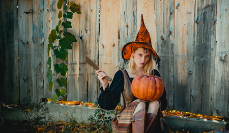 Blonde girl is preparing to carving a pumpkin. Witch posing with Pumpkin on wood background. Happy...