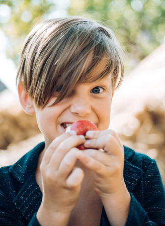 Happy child at the autumn fair. Little boy advertises natural products. Portrait of a cheerful boy lying in a hay. The boy advertises childrens clothes for the autumn.の写真素材