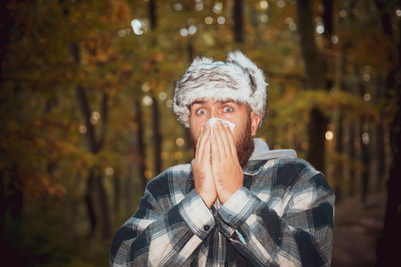 Closeup portrait of young man in autumn clothes with allergy or cold. Man work out after he Sick blowing nose and sneezing, coughing. Flu season, vaccination. Stop the flu epidemy.の写真素材