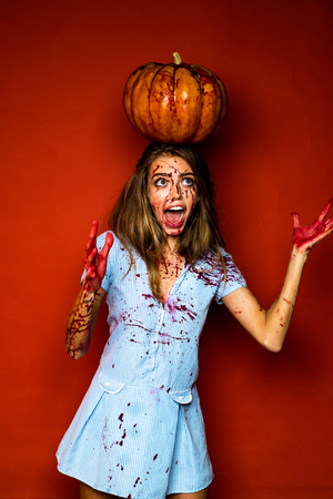 Halloween girl in blood with pumpkin. Halloween woman with a carved Pumpkin. Vampire Witch lady with blood in mouth on red background. Dress for a costume party Halloween.の写真素材