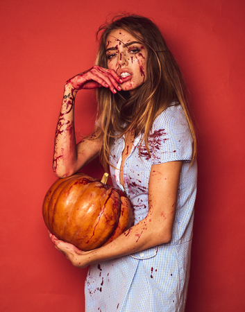 Beautiful bloody woman in costume holding pumpkin. Pretty young blonde woman clothed in dress with pumpkins. Model girl in Halloween costume and make up.の写真素材