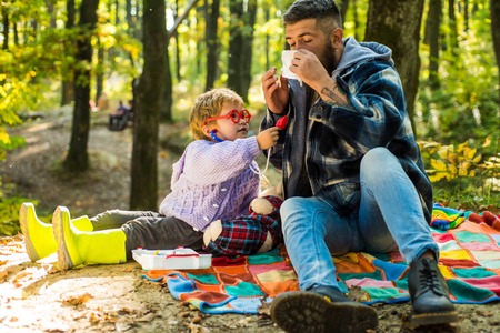 Father and son playing in the autumn forest. Sneezing young boy with nose wiper among yellow trees in park. Father and child son in autumn park having fun and laughing.の写真素材