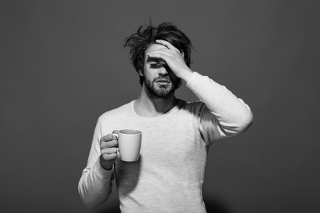 sleepy tired man with headache hold cup of teaの写真素材