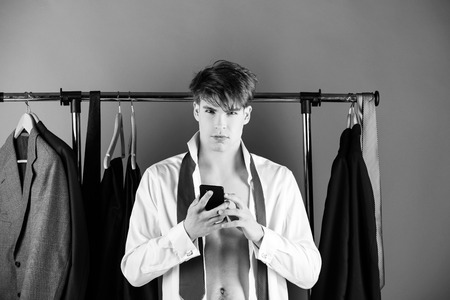 shaved man with muscular torso at wardrobe hanger with phoneの写真素材