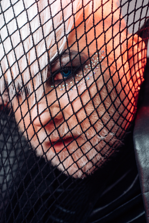 Looking at fashion at unique way. Heterosexual man with male makeup. Transgender man cover face with fishnet. Male makeup look. Fetish fashion. BDSM fashion accessoryの写真素材