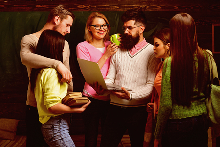Group of students, groupmates spend time with teacher, lecturer, professor. Students, scientists studying after classes, professor holds laptop, teaches , explaining. College and university conceptの写真素材