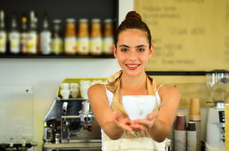 Happy and cute. Barista serve cup of hot coffee drink. Woman barista in coffee shop. Pretty woman stand behind cafe counter. Brewing coffee in coffeehouse. The best coffee recipe.の写真素材