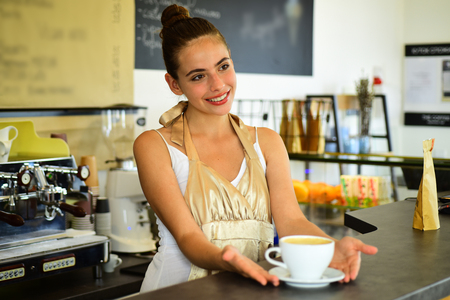 Todays good mood is sponsored by coffee. Woman barista in coffee shop. Barista serve cup of hot coffee drink with smile. Pretty woman stand behind cafe counter. Brewing coffee in coffeehouse.の写真素材