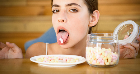 Sweet tooth. Candy girl with sweet confectionery. Pretty woman hold marshmallows on tongue. Funny woman enjoy eating marshmallows. Junk food. Unhealthy and harmful food. Sweet snack.の写真素材