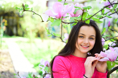 Spring mood. Adorable girl smile in park with blossoming flowers. Its spring time. Pretty girl near flowering tree enjoy magnolia blossom. Cute girl happy smiling on spring landscape.の写真素材