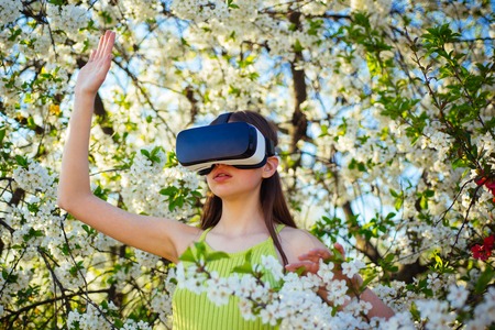 So lets fantasize. Pretty girl in virtual reality headset. Virtual technology simulation. Cute girl play in spring garden. Young lady wear vr glasses in spring bloom. Innovative vr technology.の写真素材