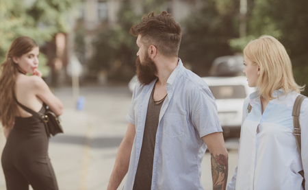 Relationship problem. Man cheating his wife or girlfriend. Bearded man looking at other girl. Hipster choosing between two women. Betrayal and infidelity. Unfaithful love. Love triangle and threesome.の写真素材