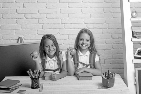 Little girls eat apple at lunch break. Friendship of small sisters in classroom at knowledge day. School time of girls. Happy school kids at lesson in september 1. Back to school and home schoolingの写真素材