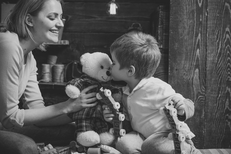 Kindness and education concept. Mother teaches son to be kind and friendly. Family play with teddy bear at home. Mom and child play with soft toy. Nursery wooden wall on background.の写真素材