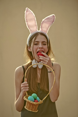 Easter woman with wicker basket biting egg on beige backgroundの写真素材