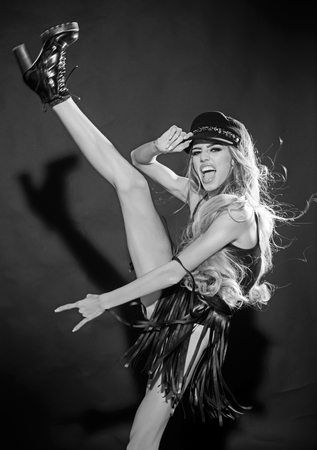 cool woman with raised leg in trendy hat and boot on black background. cool woman with happy face in studio.の写真素材