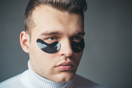 Man face with flakes under the eyes. Mans flakes. Patches under close eyes for man. Acupressure, massage his temples, flakes collagen.の写真素材