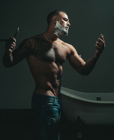 Hairdressers work for a handsome guy at the barber shop. Man visiting hairstylist in barber shop. Beard balm. Shaving man and razor man. Barber shaving a bearded man in a barber shop.の写真素材