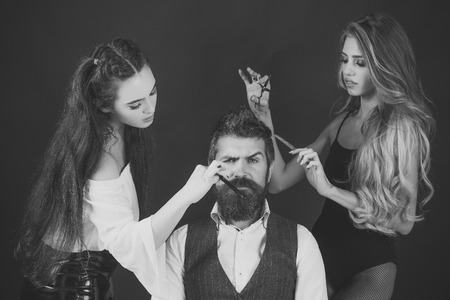 Barbershop, fashion, beauty, hipster. Bearded man, sexy women with long hair. Friends at hairdresser salon, lgbt. People make haircut, love relations, friendship. Women with comb, scissors cut hair.の写真素材