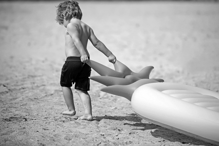 Small boy child pull air mattress on sand. Summer vacation and travel to ocean. Pineapple inflatable mattress, activity and joy. Maldives or Miami beach. little kid on Caribbean sea in Bahamasの写真素材