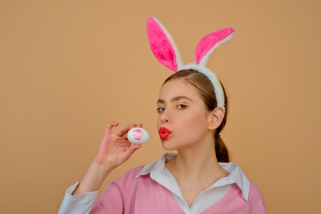 Lips and Easter, Lipstick kiss imprint on easter egg. Happy easter. Young woman in rabbit bunny ears. Portrait of a happy woman in bunny ears. Egg hunt.の写真素材
