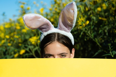 Beautiful young woman with bunny ears and blank poster on outdoor background. Copy space. Easter holiday concept. Discount.の写真素材