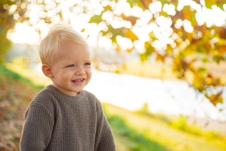 Toddler boy blue eyes enjoy autumn. Small baby toddler on sunny autumn day. Warmth and coziness. Happy childhood. Sweet childhood memories. Child autumn leaves background. Warm moments of autumnの写真素材