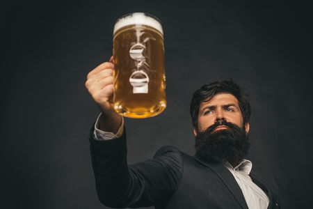 Handsome barman holding a pint of beer. Hipster relaxing at pub. Bearded man with a glass of beer.の写真素材