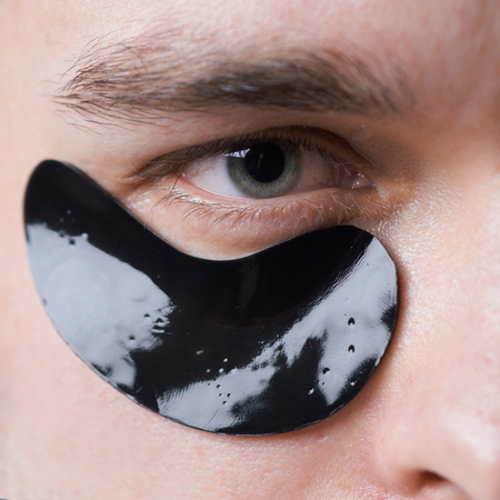 Black pearl extract. Skin care. Minimizes puffiness and reduce dark circles. Eye patches for men. Man with black eye patches close up. Metrosexual concept. Focused treatments for under eye areaの写真素材