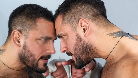 A mirror where a man watching himself. Man and mirror. Bearded hispanic man pointing finger at mirror. Brutal latino man with beard and mustache looking at his reflection in mirrorの写真素材