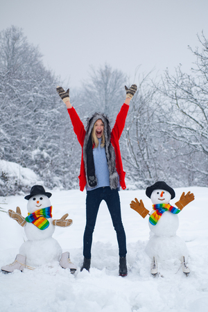 Funny snowman in stylish hat and scarf with funny girl on snowy field. Happy girl plaing with a snowman on a snowy winter walk. Happy girl snowman and winter fun.の写真素材