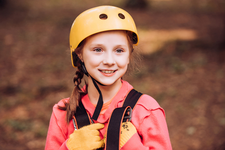 Little child climbing in adventure activity park with helmet and safety equipment. Happy child climbing in the trees. Cute child boy. Happy child boy calling while climbing high tree and ropes.の写真素材