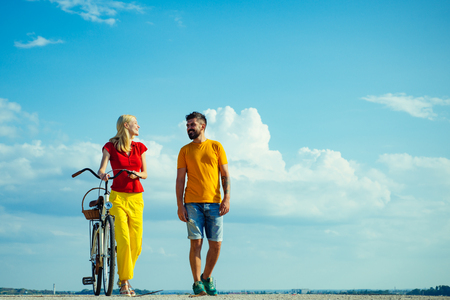 Sky background for your text. Beautiful summer day. Summer vacation. Enjoying time together. Summer couple. Couple in summer dress rides a bike. Talking. Blue sky background - copy space.の写真素材