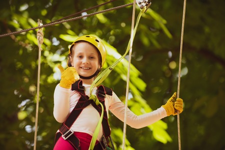 Rope park - climbing center. Artworks depict games at eco resort which includes flying fox or spider net. Hiking in the rope park girl in safety equipment. Roping park. Child.の写真素材
