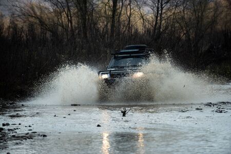 Off road vehicle coming out of a mud hole hazard, mud and water splash in off-road racing. Scene of...